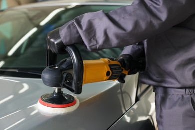 Photo of Man polishing car hood with orbital polisher indoors, closeup