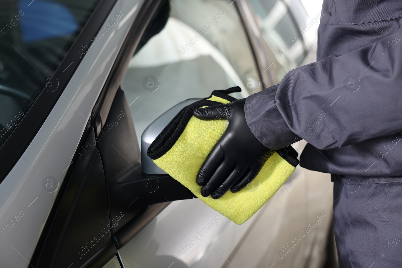 Photo of Man cleaning car side view mirror with yellow rag indoors, closeup