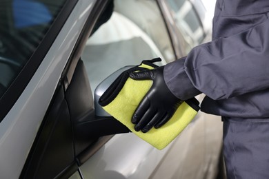 Photo of Man cleaning car side view mirror with yellow rag indoors, closeup