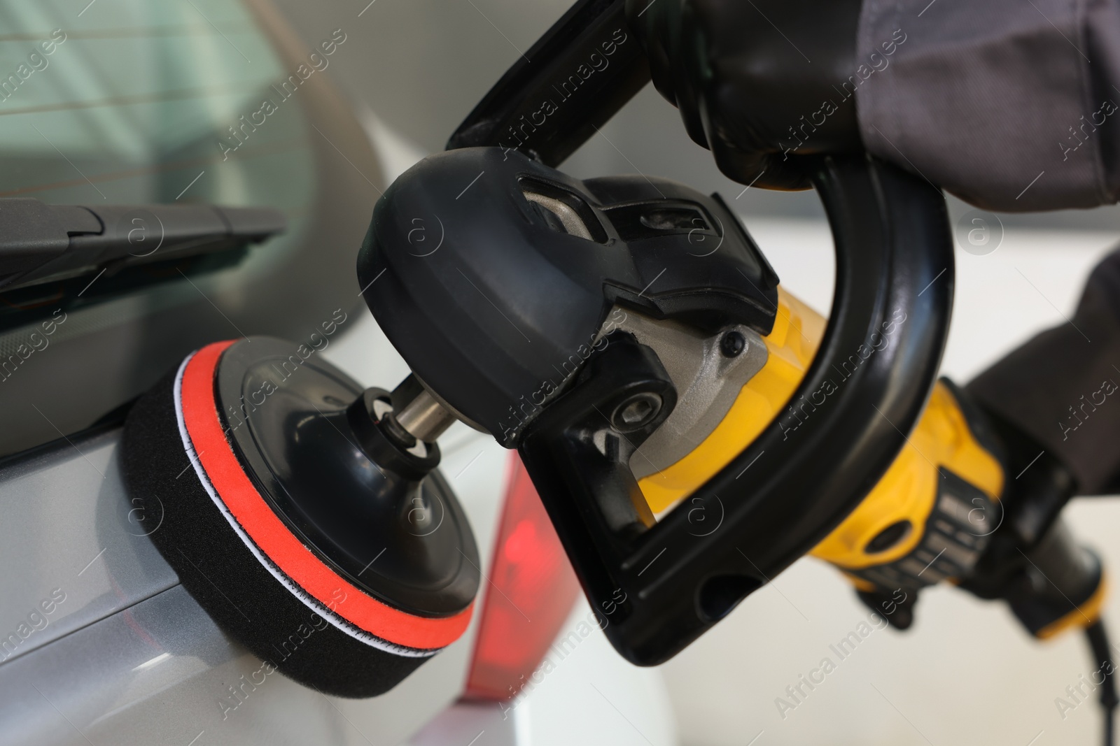 Photo of Man polishing car with orbital polisher indoors, closeup