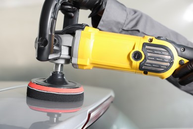 Photo of Man polishing car with orbital polisher indoors, closeup