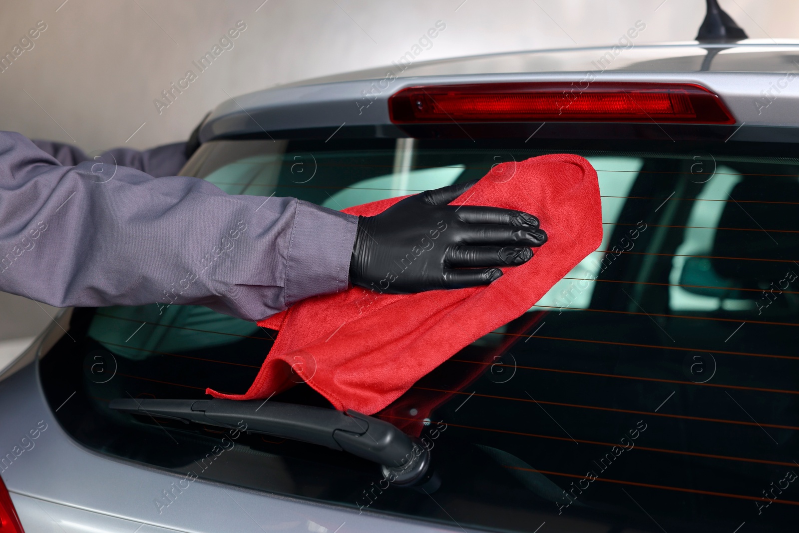 Photo of Man polishing car rear window with red rag indoors, closeup