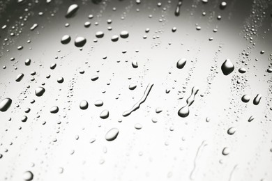 Water drops on light grey glass surface, closeup