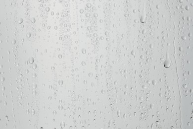 Photo of Water drops on light grey glass surface, closeup