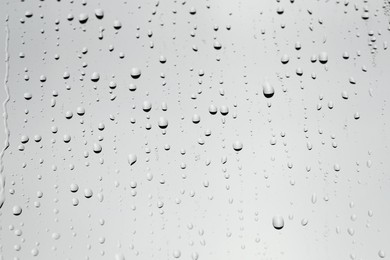 Photo of Water drops on light grey glass surface, closeup