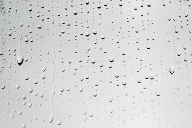 Water drops on light grey glass surface, closeup