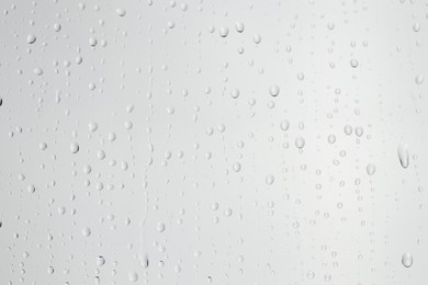 Photo of Water drops on light grey glass surface, closeup