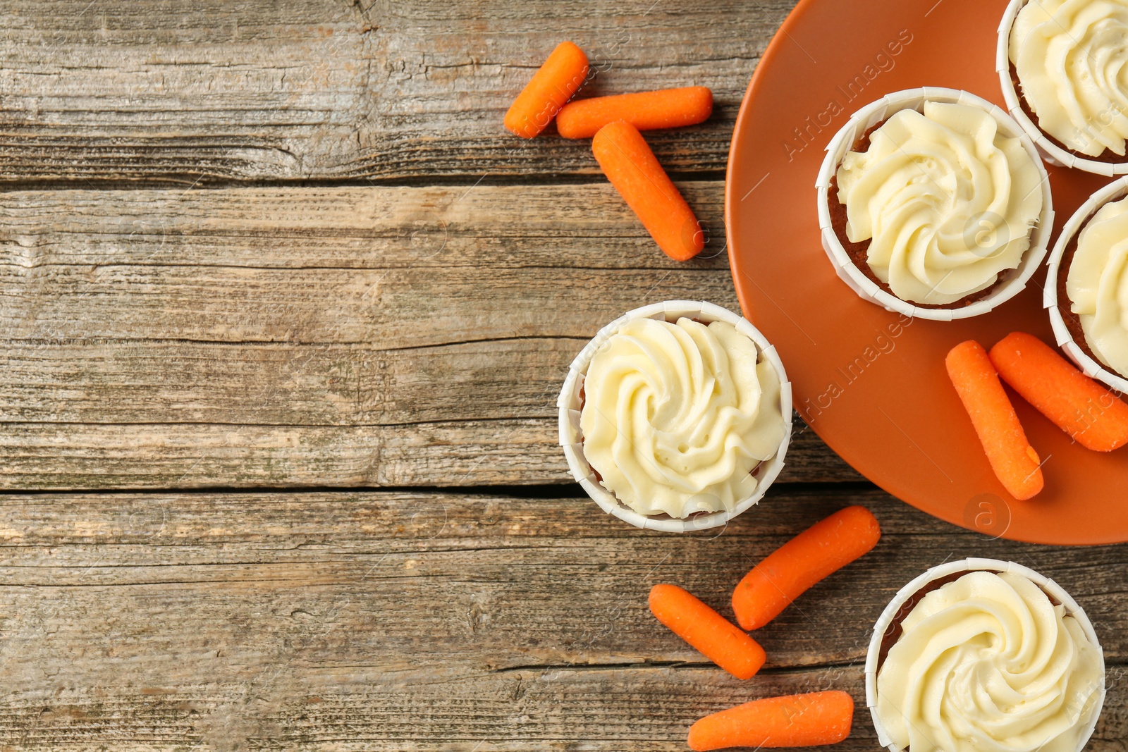 Photo of Delicious carrot muffins and fresh vegetables on wooden table, flat lay. Space for text