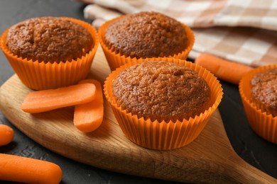 Photo of Delicious carrot muffins with fresh vegetables on black table, closeup