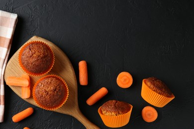 Photo of Delicious carrot muffins with fresh vegetables on black table, flat lay. Space for text