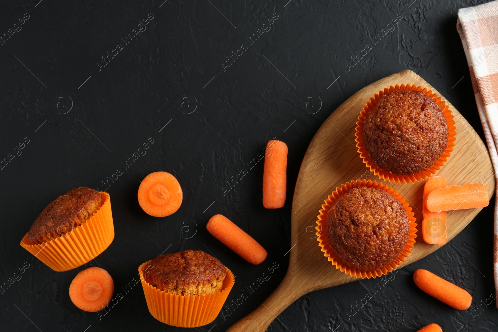 Photo of Delicious carrot muffins with fresh vegetables on black table, flat lay. Space for text