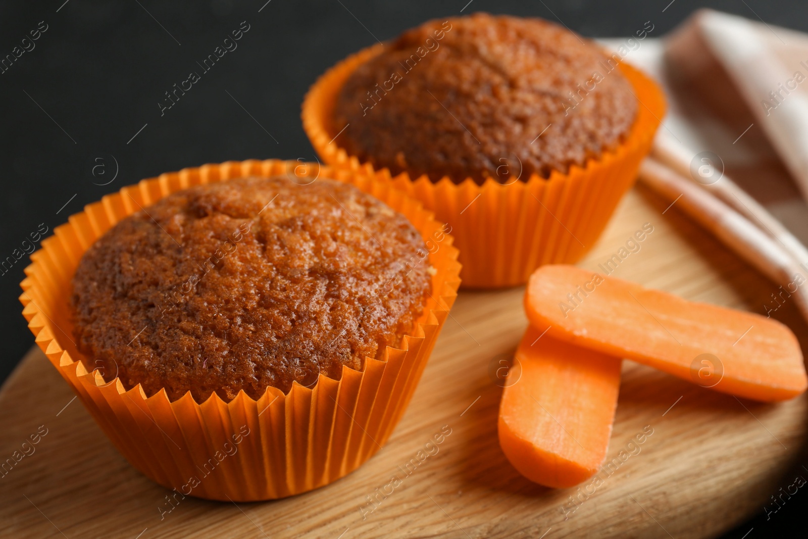 Photo of Tasty carrot muffins with fresh vegetable on black table, closeup