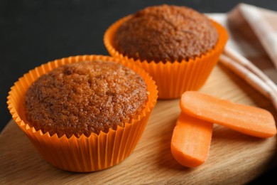 Photo of Tasty carrot muffins with fresh vegetable on black table, closeup