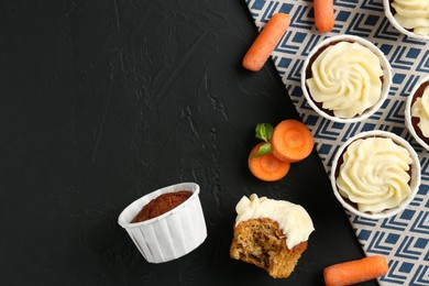 Photo of Delicious carrot muffins with fresh vegetables on black table, flat lay. Space for text