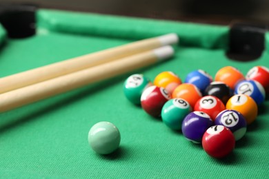 Photo of Billiard balls in triangle and cues on green table indoors, closeup