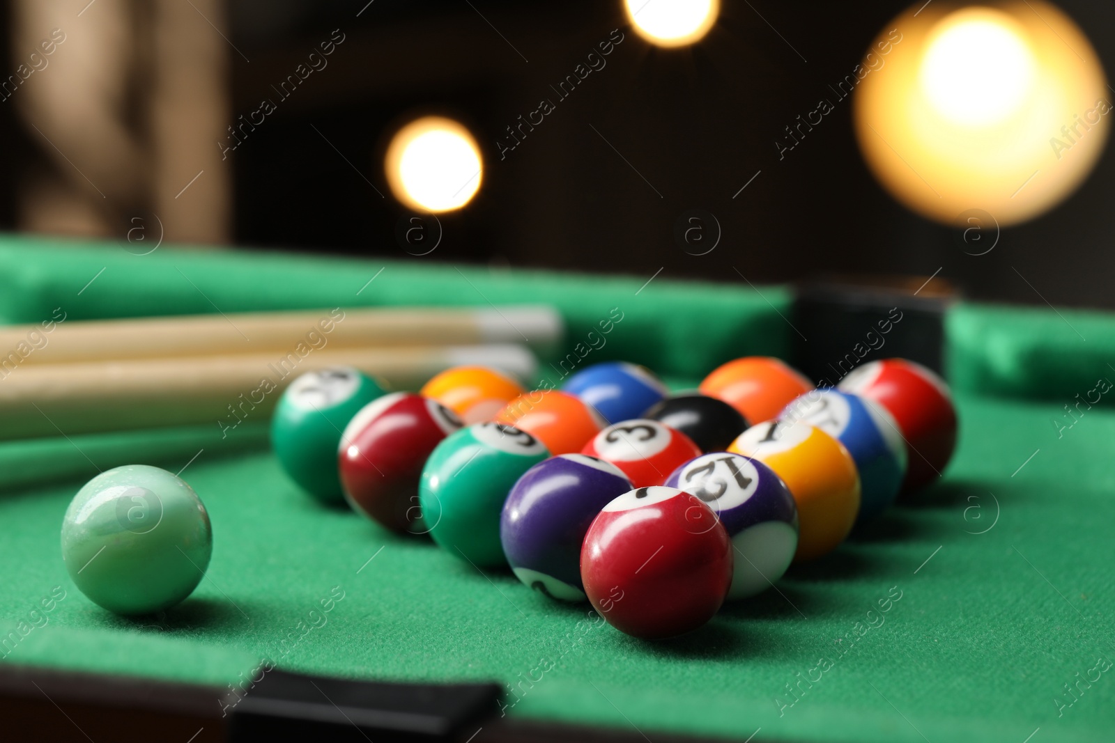 Photo of Billiard balls in triangle and cues on green table indoors, closeup