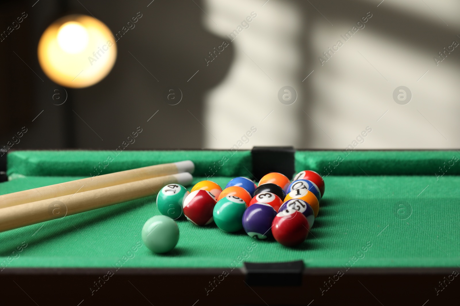 Photo of Billiard balls in triangle and cues on green table indoors. Space for text