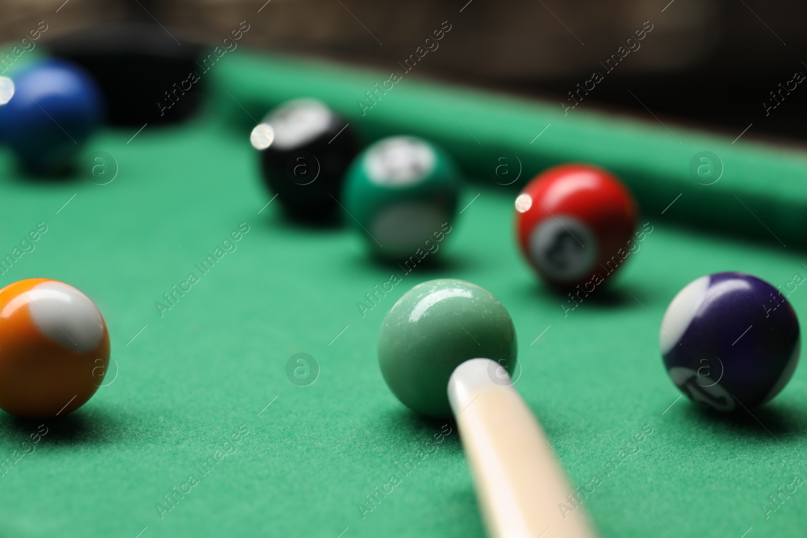 Photo of Many colorful billiard balls and cue on green table indoors, closeup