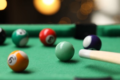 Photo of Many colorful billiard balls and cue on green table indoors, closeup