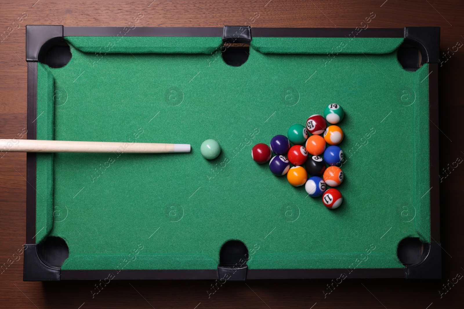 Photo of Billiard balls in triangle and cue on green table, top view