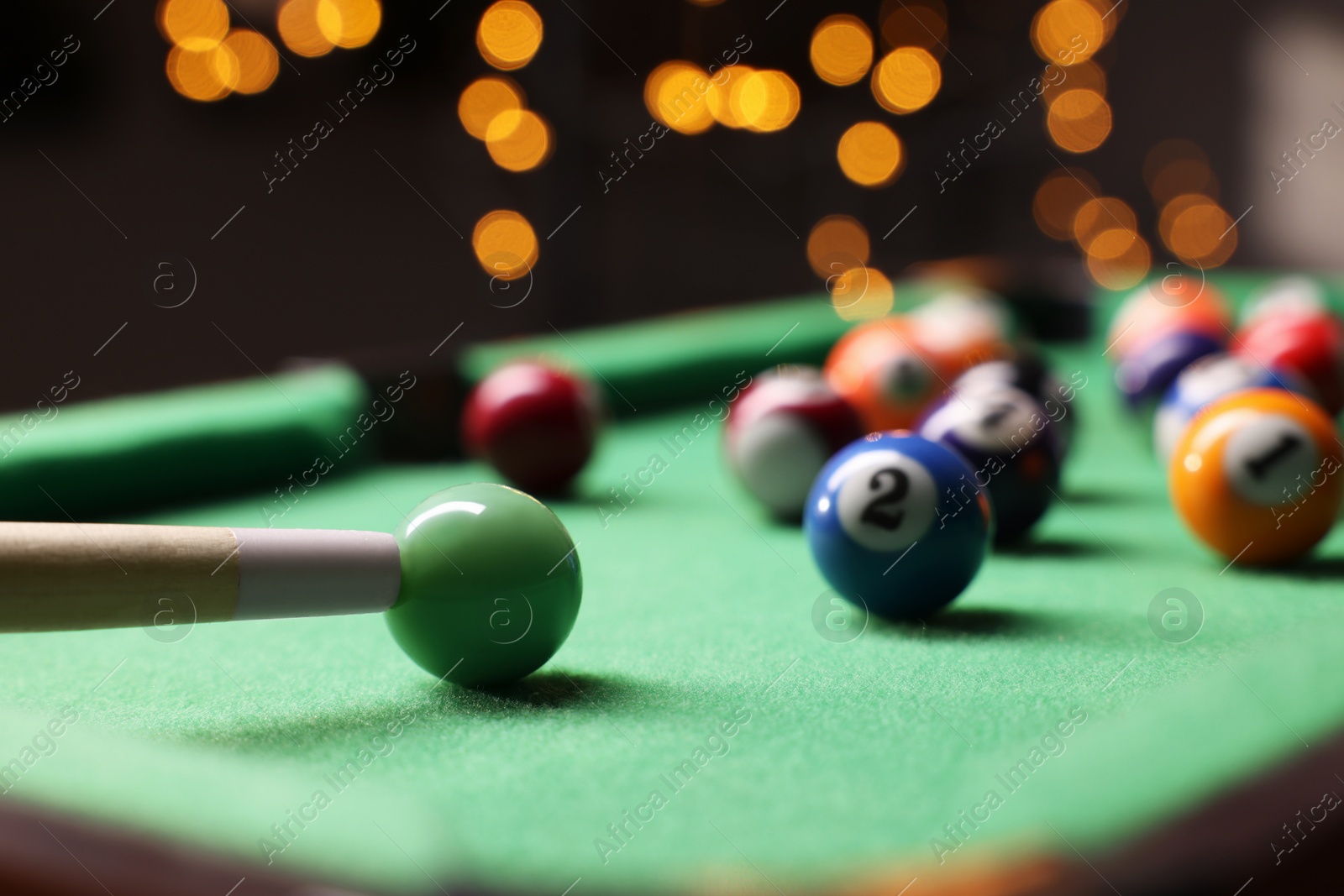 Photo of Many colorful billiard balls and cue on green table indoors, closeup