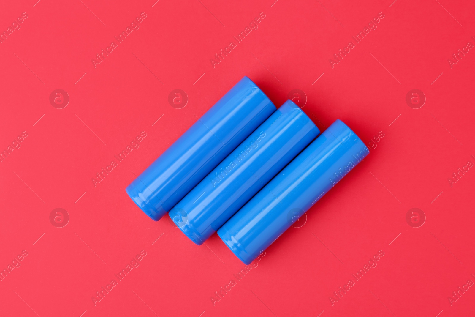 Photo of Three AA cell batteries on red background, top view