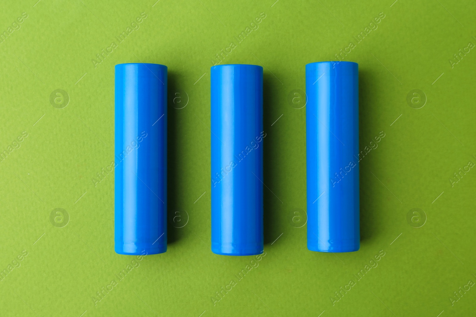 Photo of Three AA cell batteries on green background, top view