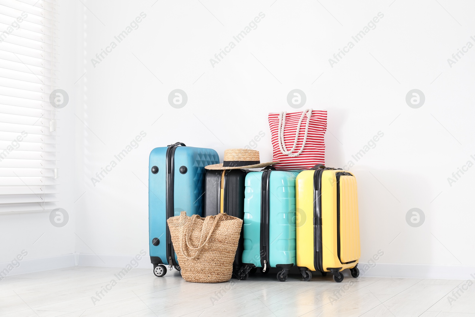 Photo of Colorful suitcases, beach bags and straw hat on floor near white wall