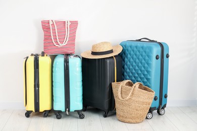 Photo of Colorful suitcases, beach bags and straw hat on floor near white wall