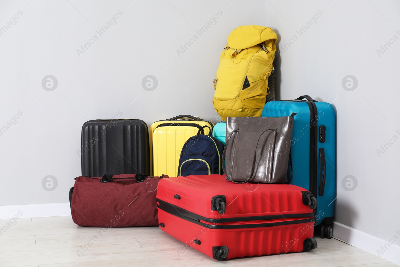 Photo of Colorful suitcases, backpacks and bags on floor near light wall