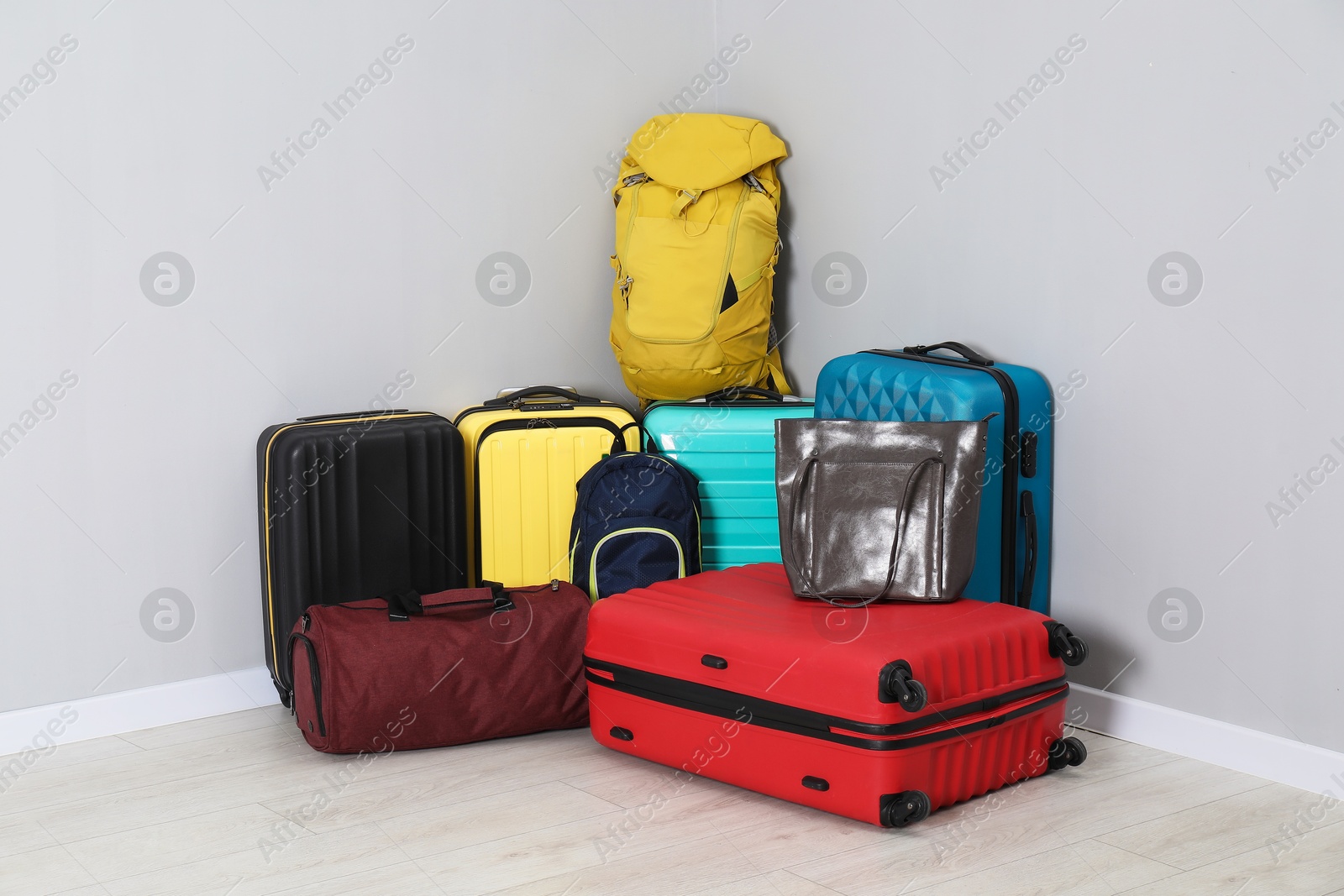 Photo of Colorful suitcases, backpacks and bags on floor near light wall