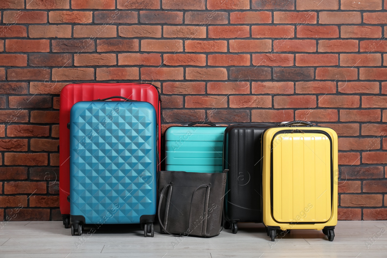 Photo of Many colorful suitcases and bag on floor near brick wall