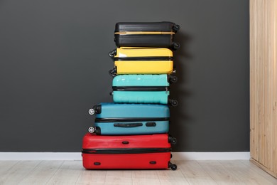 Photo of Stack of colorful suitcases on floor near black wall