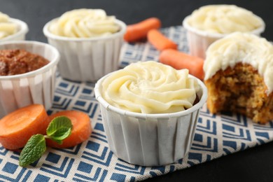 Photo of Delicious carrot muffins with fresh vegetables on black table, closeup