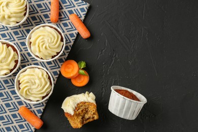 Photo of Delicious carrot muffins with fresh vegetables on black table, flat lay. Space for text