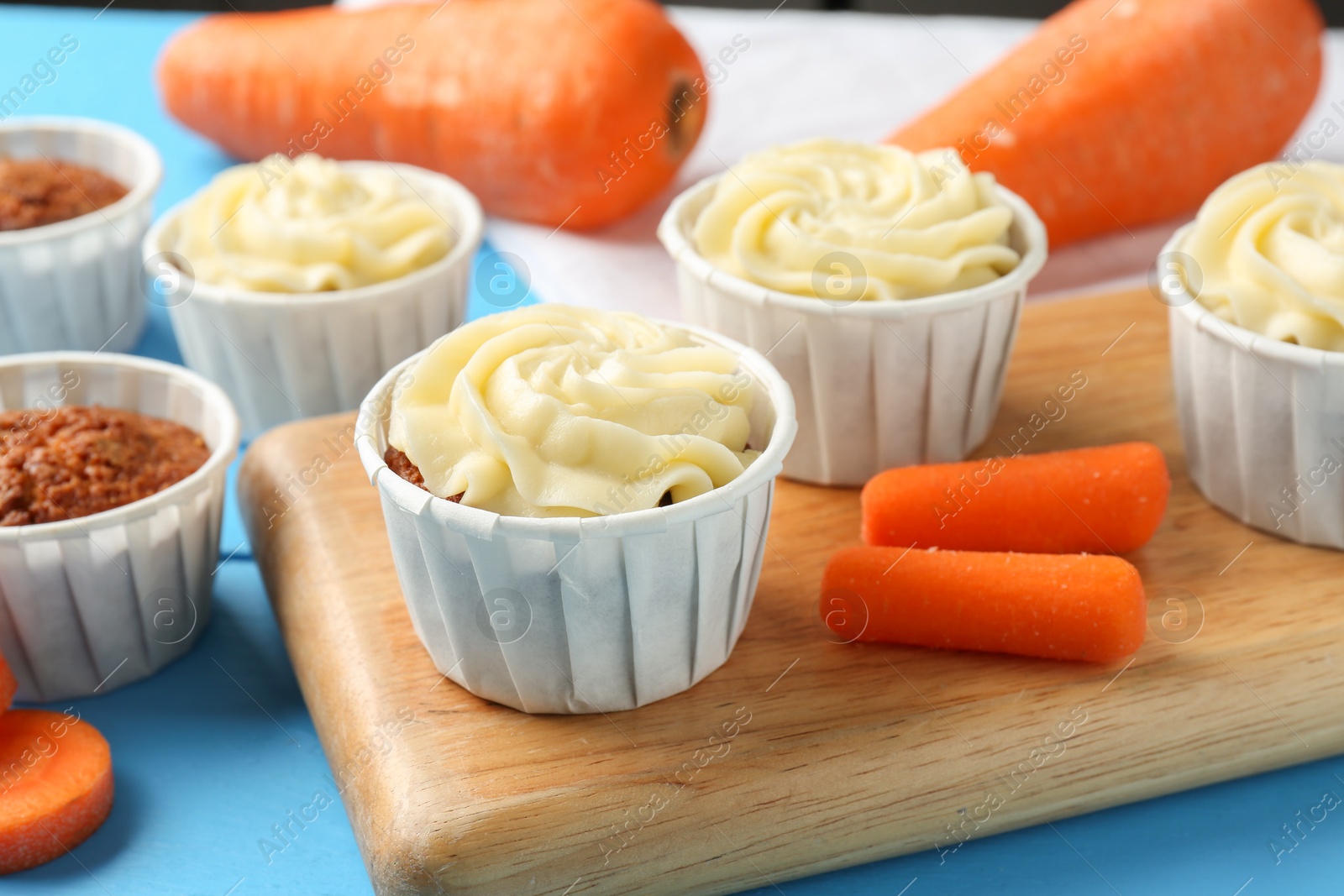 Photo of Tasty carrot muffins with fresh vegetables on light blue table, closeup