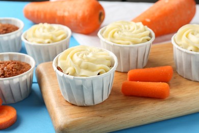 Photo of Tasty carrot muffins with fresh vegetables on light blue table, closeup