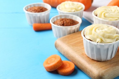 Photo of Tasty carrot muffins with fresh vegetables on light blue wooden table, closeup. Space for text