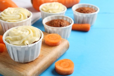 Photo of Tasty carrot muffins with fresh vegetables on light blue wooden table, closeup. Space for text