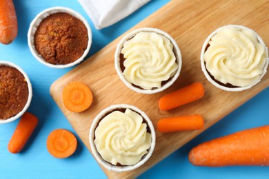 Photo of Tasty carrot muffins with fresh vegetables on light blue wooden table, flat lay