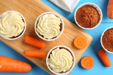 Photo of Tasty carrot muffins with fresh vegetables on light blue wooden table, flat lay