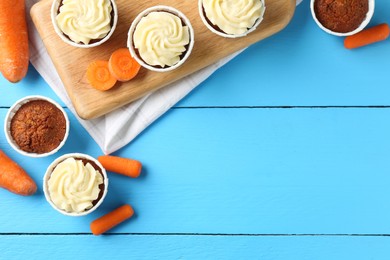 Photo of Tasty carrot muffins with fresh vegetables on light blue wooden table, flat lay. Space for text