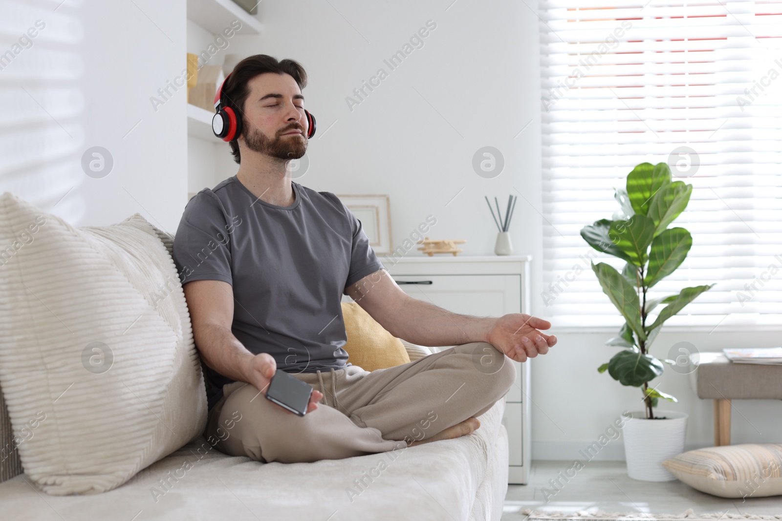 Photo of Handsome man in headphones with smartphone meditating on sofa at home