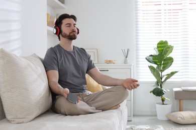 Photo of Handsome man in headphones with smartphone meditating on sofa at home