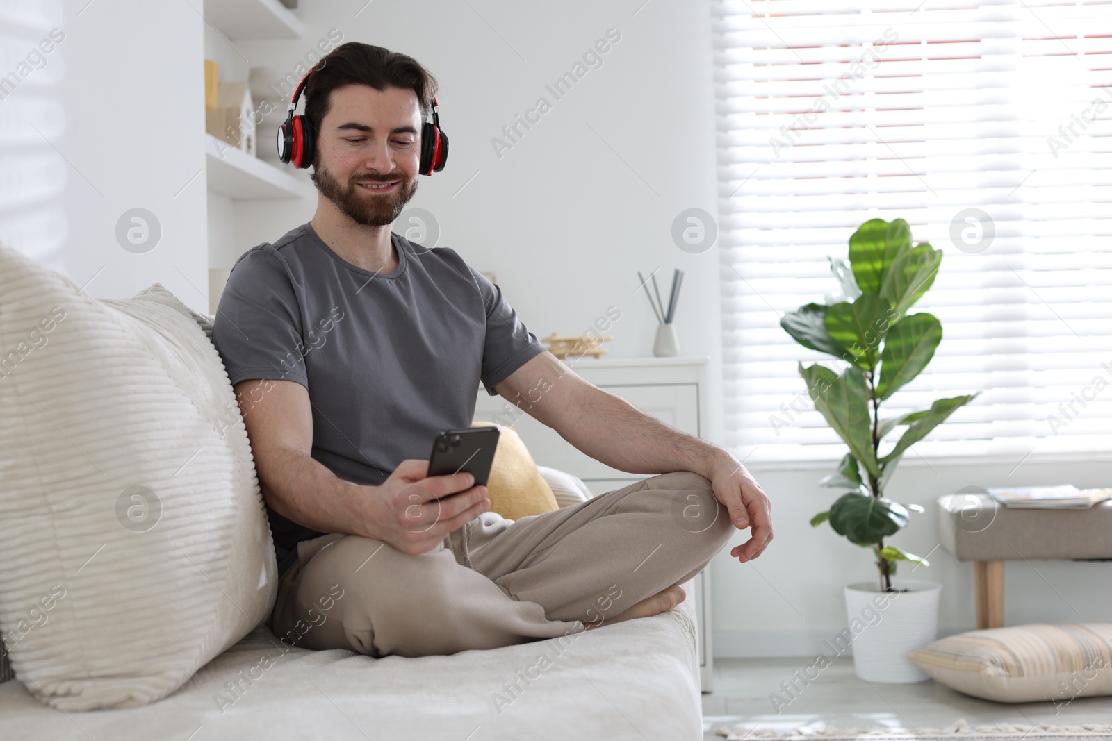 Photo of Smiling man in headphones with smartphone meditating on sofa at home