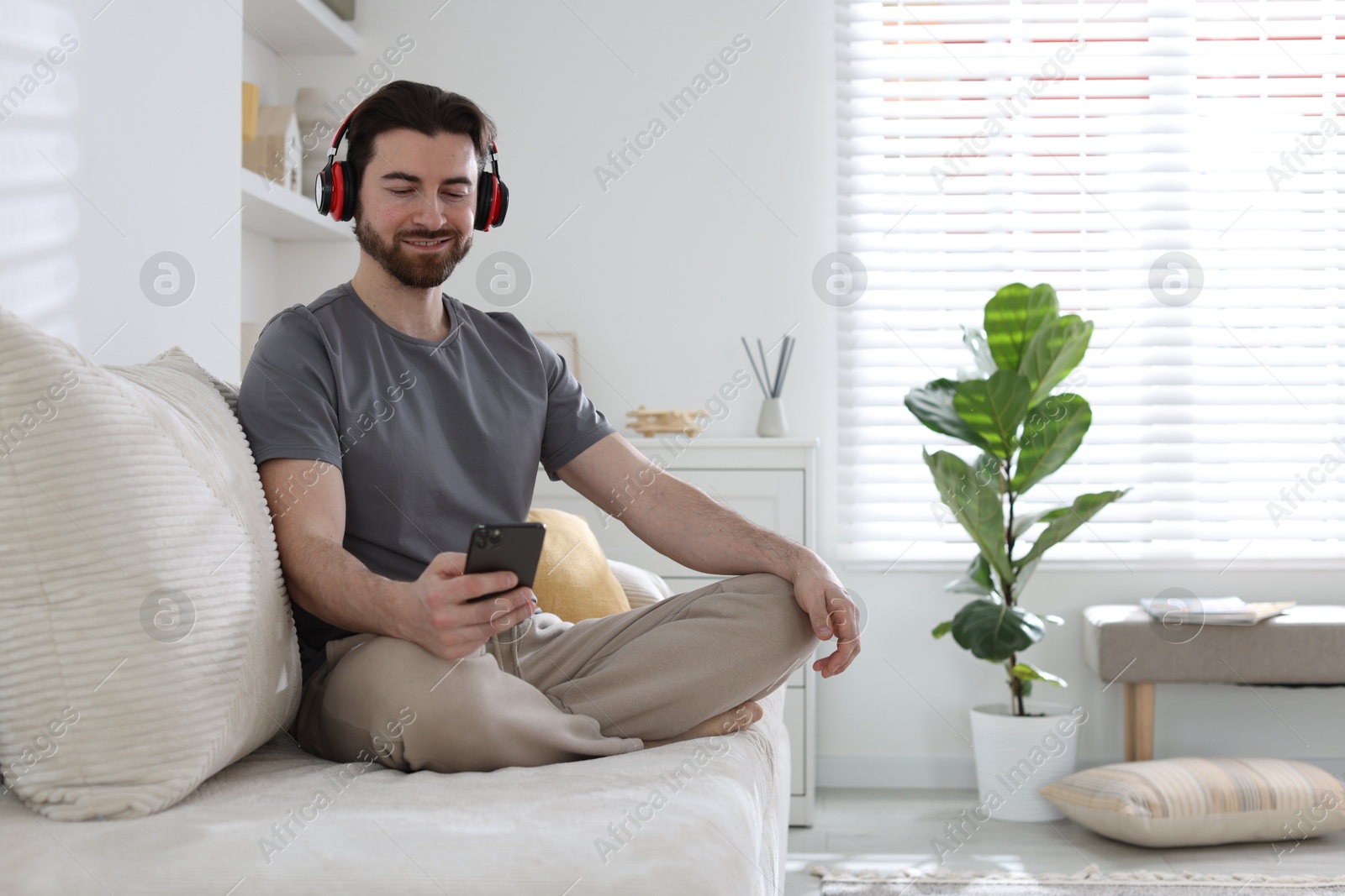 Photo of Smiling man in headphones with smartphone meditating on sofa at home