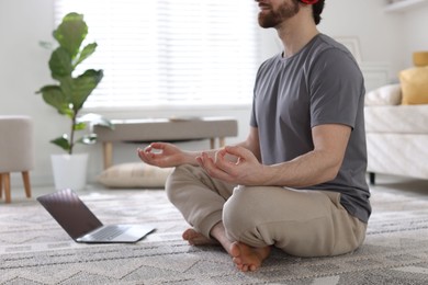 Photo of Man with laptop meditating on floor at home, closeup