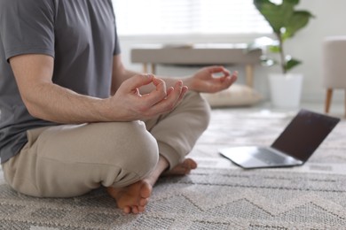 Photo of Man with laptop meditating on floor at home, closeup