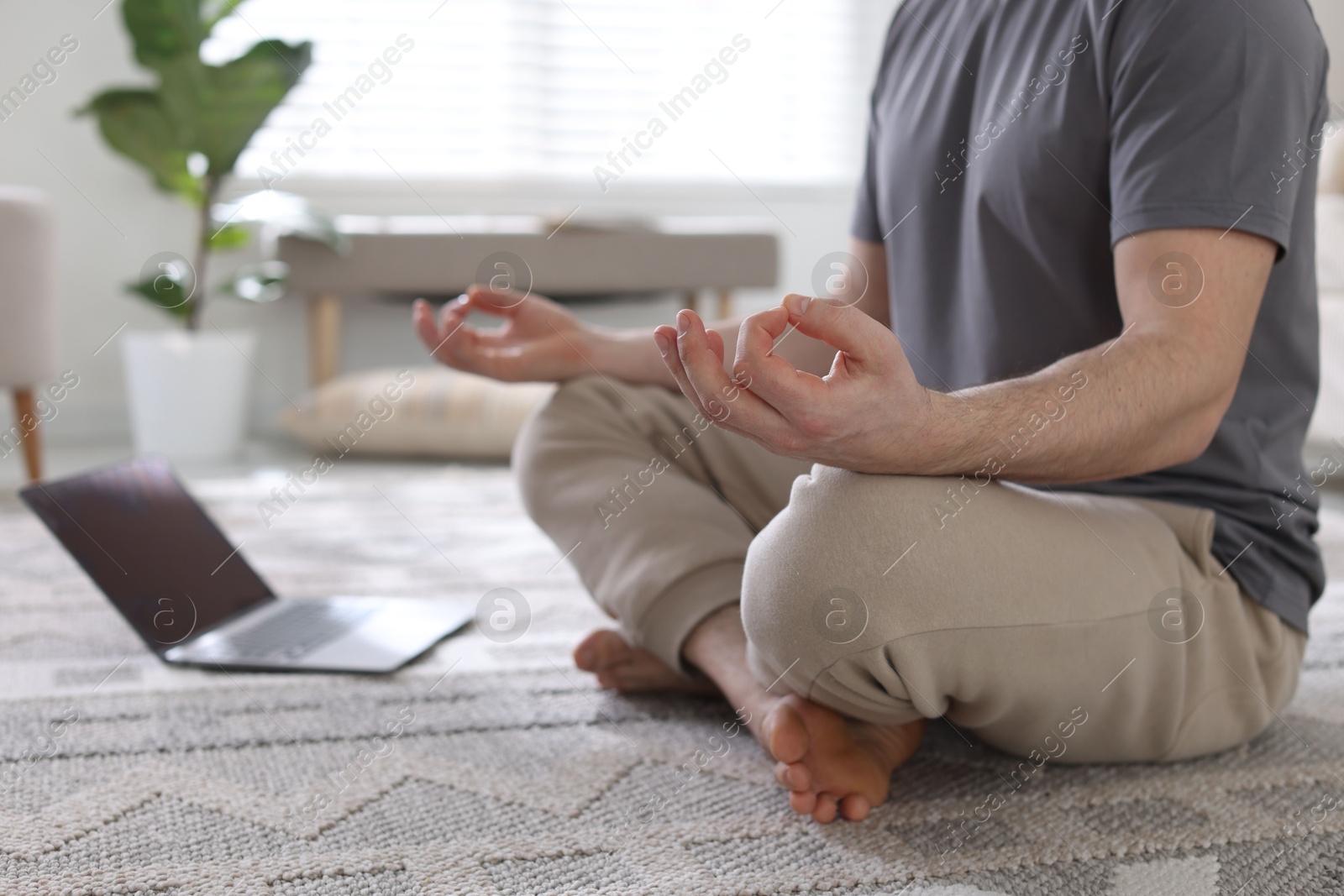 Photo of Man with laptop meditating on floor at home, closeup