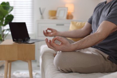 Photo of Man meditating near laptop on sofa at home, selective focus